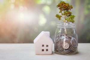 Property or real estate investment. Home mortgage loan rate. Reflection of tree plant growing out of coins in glass jar and house model on table. Real estate passive income